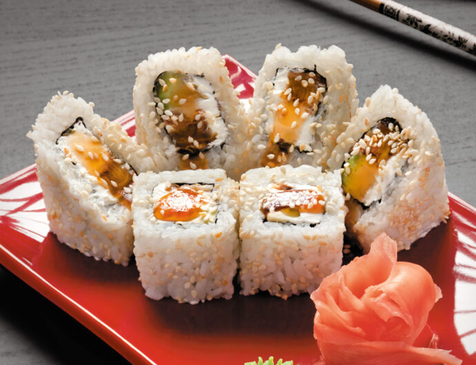 A studio close-up of chopsticks and a square plate with six pieces of eel sushi, wasabi and ginger.